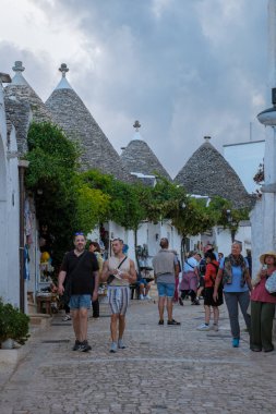 Alberobello İtalya 18 Eylül 2024 Puglia 'nın büyüleyici caddelerinde gezinen ziyaretçiler, yeşillikle süslenmiş ikonik trulli hayran hayran, sakin bir akşamda canlı bir atmosfer yaratıyor