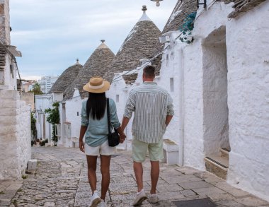 Bir çift el ele yürür Alberobello Puglia 'nın pitoresk sokaklarında. Geleneksel trulli evlerle çevrili bu büyüleyici yeri keşfetmek için huzurlu bir anın tadını çıkarıyorlar.