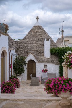 Alberobello, Puglia 'da geleneksel trullo evlerinin çiçek açan çiçeklerle çevrili ikonik konik çatılarını sergilediği tuhaf bir avluda geziniyor. 