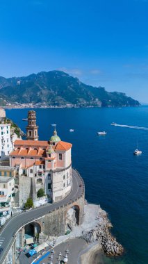 Majestic cliffs rise above the charming buildings of the Amalfi Coast, as boats gently glide across the tranquil blue waters under a brilliant sky, Atrani Italy clipart