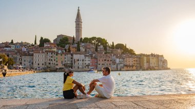 Güneş Rovinj 'in üzerinde batarken, birkaç tanesi köpüklü suyla rahatlıyor, gökyüzünün canlı renklerinden ve sahil kasabasının resimli binalarından etkileniyor..