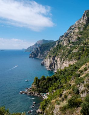 Breathtaking cliffs rise sharply from the serene turquoise waters along the Amalfi Coast, revealing lush greenery and charming coves under a clear blue sky. A perfect day in Italy unfolds. clipart