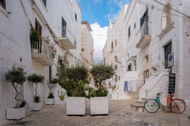 Ostuni Italy 18 September 2024, A charming alley in Puglia, Italy, reveals whitewashed buildings beside leafy planters, while clothes dry in the sunlight clipart