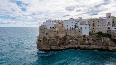 Kayalık bir uçuruma tünemiş, Puglia 'nın pitoresk köyü, tepemizde dramatik bulutlar, Polignano a Mare Italy gibi parıldayan mavi denize bakan, beyazlatılmış binalarla övünüyor. 