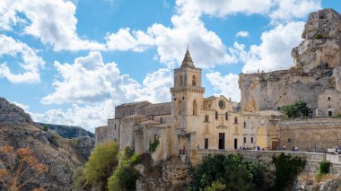 In the heart of Matera, Puglia,Italy the ancient stone buildings rise majestically, framed by a brilliant blue sky and puffy clouds. The rich history blends seamlessly with the breathtaking landscape. clipart