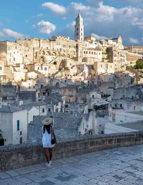 Sıcak güneş ışığında güneşlenen bir gezgin, Matera İtalya 'nın yamaçlarında büyülenmiş bir kaya çıkıntısının üzerinde duruyor. Kayalara oyulmuş tarihi binalar kasabanın eşsiz cazibesini ve güzelliğini gözler önüne seriyor..