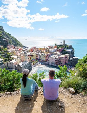 Huzurlu bir gözcüden, iki gezgin canlı uçurum kenarındaki Cinque Terre köyüne hayran kalarak, yumuşak güneş ışığı ve ışıl ışıl denizde dans eden hafif meltemler altında güneşleniyor. Vernazza İtalya