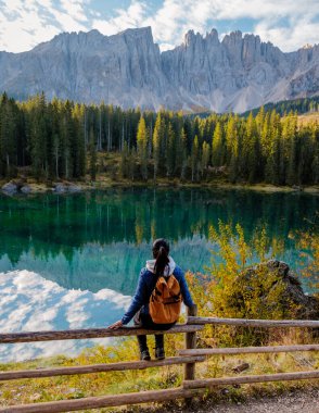 Dolomitler 'in içine yerleşmiş, ışıl ışıl bir gölün kıyısındaki bir gezgin. Etrafı canlı sonbahar yaprakları ve suda yansıyan görkemli dağlarla çevrili. İtalya 'da Carezza Gölü veya Karersee Dolomitleri.