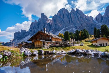 Parlak yeşillik ve sonbahar yapraklarıyla çevrili berrak bir gölet ile sakin bir çadırın üzerinde görkemli zirveler yükselir. İtalya 'da Geisleralm Dolomitleri Val Di Funes Puez Odle Doğa Parkındaki Adolf Munkel Patikası