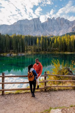 Zümrüt yeşili bir göl olan görkemli Dolomite tepeleri ve canlı sonbahar yapraklarıyla çevrili bir çift, huzurlu bir anın tadını çıkarıyor. İtalya 'da Carezza Gölü veya Karersee Dolomitleri.