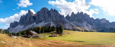 Canlı sonbahar yapraklarıyla kaplı büyüleyici ahşap kulübelerin üzerinde nefes kesici dağlar belirgin bir şekilde yükselir. İtalya 'da Geisleralm Dolomitleri Val Di Funes Puez Odle Doğa Parkındaki Adolf Munkel Patikası