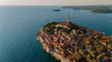 Gök mavisi sular boyunca uzanan Rovinj, resimli binaları ve canlı çatılarıyla büyülenirken, güneş batıyor ve sakin manzaranın üzerine sıcak bir parıltı saçıyor..