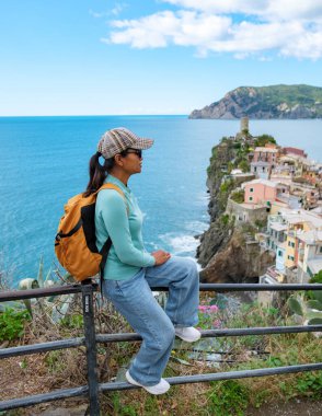 Bir gezgin, İtalya 'nın Cinque Terre kentinin çarpıcı manzarasını seyrediyor, korkuluklara karşı sessizce oturuyor. Mavi sular ve renkli binalar manzaralı bir zemin oluşturuyor, Vernazza İtalya