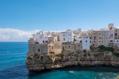 Polignano a Mare Italy Parlak güneş ışığı Puglia 'nın büyüleyici beyaz binalarını aydınlatıyor, kayalık kayalıklara tünemiş.