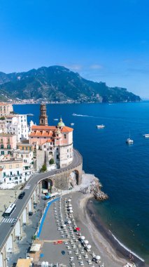 Amalfi Sahili 'nin nefes kesici manzarası, berrak bir gökyüzünün altındaki sakin suları teknelerin doldurduğu ışıl ışıl mavi denizin üzerinde tünemiş pitoresk bir köyü gözler önüne seriyor. Güneş yatakları güzel kumsalda..