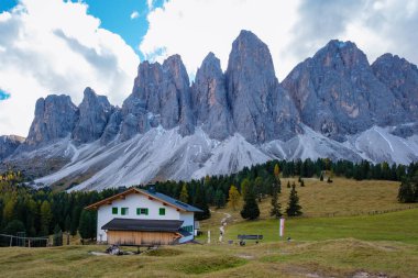 Çimenli vadiye yerleşmiş büyüleyici bir dağ evi Dolomitlerin dramatik arka planına karşı duruyor. Yeşillik ve yükselen zirveler, İtalya 'daki Dolomitler Val Di Funes Adolf Munkel Patikası