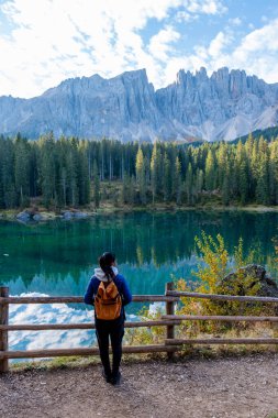 Huzurlu bir gölün kenarında duran bir yürüyüşçü Dolomitlerin nefes kesici manzarasına hayran kalır. İtalya 'daki Carezza Gölü ya da Karersee Dolomitleri' nin sakin sularında yansıyan uzun tepeler görkemli bir şekilde yükselir..