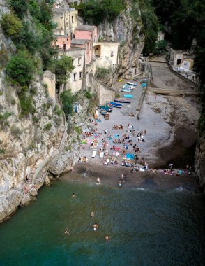 Sunbathers enjoy the picturesque hidden beach on the Amalfi Coast, surrounded by rocky cliffs and charming buildings. Fiordo Di Furore, The Furore beach Amalfi coast clipart