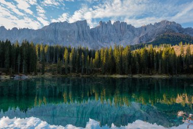 Kristal berrak sular, canlı bir gökyüzünün altında yemyeşil ormanlarla çevrili Dolomitlerin görkemli tepelerini yansıtır. İtalya 'da Carezza Gölü veya Karersee Dolomitleri.