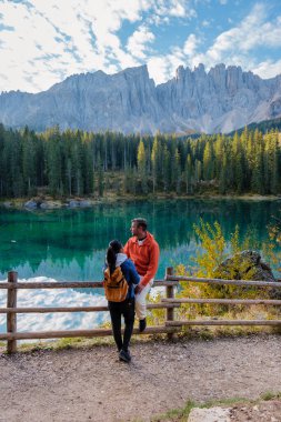 Büyüleyici bir zümrüt gölünün yanında duran bir çift, yüksek dağlar ve sonbahar yapraklarıyla çevrili. İtalya 'da Carezza Gölü veya Karersee Dolomitleri.