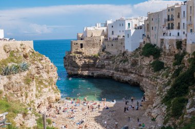 Polignano 'nun büyüleyici sahil kasabası Mare Italya' da, güneş banyosu yapanlar kayalık sahilde toplanıyor, güneşin sıcaklığını emerken turkuaz dalgalar yakındaki bir yere çarpıyor..