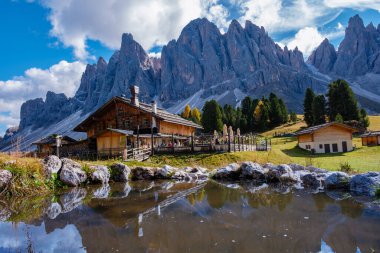 Dolomitler 'de sakin bir sonbahar günü, görkemli zirvelerle çerçevelenmiş yansıtıcı bir göletin yanında kırsal bir kulübe sergileniyor. İtalya 'da Geisleralm Dolomitleri Val Di Funes Adolf Munkel Patikası 