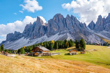 Granite peaks of the Dolomites above lush green meadows, autumn hues as traditional wooden chalets. Geisleralm Dolomites Val Di Funes in Italy Adolf Munkel Trail in Puez Odle Nature Park clipart