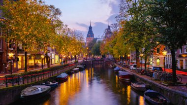 Alacakaranlık Amsterdam 'a inerken, kanallar sonbahar yapraklarının altın tonlarını ve sıcak sokak ışıklarını yansıtıyor..