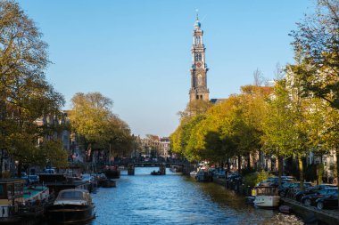 Altın yapraklar, Amsterdam 'ın sakin kanallarını kaplayan ağaçlardan yavaşça süzülüyor. Westerkerk ikonik kulesi, bir sonbahar gününün özünü yakalayarak, teknelerin huzur içinde yüzmesi gibi dimdik ayakta duruyor. 