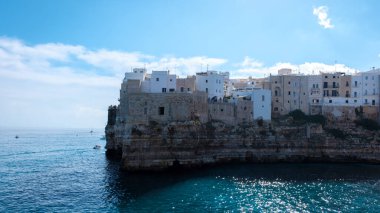 Ziyaretçiler Puglia 'nın soluk soluğa kalan uçurumlarına hayret ederken, kayalık kıyılara tutunan beyaz boyalı binalar, antik kayalara doğru hafif dalgalar, Polignano a Mare İtalya 