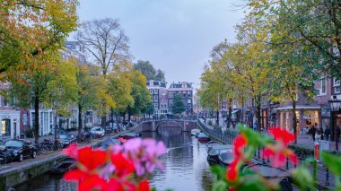 Amsterdam 23 Ekim 2024, alacakaranlık Amsterdam üzerine çökerken, kanallar parlak sonbahar renklerini yansıtıyor. Altın yapraklı ağaçlar su yollarında, büyüleyici binalar ve demirli tekneler..