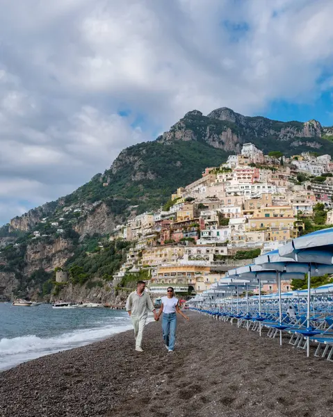 Bir çift, Amalfi Sahili üzerinde batan güneşin zeminine karşı renkli uçurum kenarındaki evlerin yükseldiği Positano 'nun görkemli çakıl taşı plajı boyunca el ele yürür..