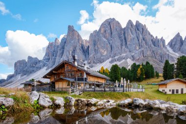 Sonbahar renklerinin canlı manzarayı geliştirdiği, yüksek Dolomite tepelerinin eteklerine kurulmuş pitoresk bir kulübe. İtalya 'da Geisleralm Dolomitleri Val Di Funes