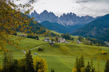 Yuvarlanan yeşil tepeler görkemli Dolomitlere karışıp nefes kesici bir zemin oluşturuyor. Tuhaf köyler manzarayı süslüyor, Santa Maddalena Val di Funes İtalya