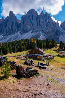 Ziyaretçiler, göz kamaştırıcı dağ zirveleri ve canlı sonbahar yapraklarıyla çevrili pitoresk Dolomitlerin keyfini çıkarıyorlar. İtalyan Puez Odle Doğa Parkı 'ndaki Geisleralm Dolomitleri Val Di Funes.