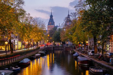 Alacakaranlık Amsterdam 'ı sararken, köprülerin ve binaların sıcak ışıklarını yansıtan, sakin kanalların üzerinde altın yapraklar çırpınıyor..