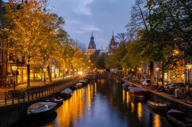 Alacakaranlık Amsterdam 'a inerken, kanallar ağaçların ve binaların sıcak ışıklarını yansıtıyor. Su yollarında kayıkla gezerken, bu sahne sonbaharın canlı renkleri ve sakin atmosferiyle büyülenir..