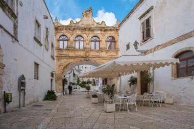 18 Eylül 2024 'te Puglia' da gezinen Ostuni İtalya 'da ziyaretçiler tarihi mimariyle süslenmiş hoş bir caddeye rastladılar. Güzel bir kemer, açık havada rahat bir kafe olan meydanı çerçeveler.