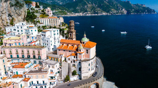 Nestled against steep cliffs, colorful homes line the Amalfi Coast, creating a captivating vista as boats gently drift along the sparkling sea. The morning sun casts a warm glow on this Italian gem.
