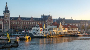 Amsterdam 23 Ekim 2024. Sonbaharda Amsterdam Merkez İstasyonu 'nda güneş batarken ılık parıltısı su yollarını ve tarihi binaları aydınlatıyor.