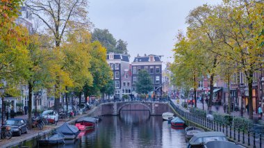 Amsterdam 23 Ekim 2024, Altın sonbahar yaprakları Amsterdam 'ın sakin kanallarını çerçeveliyor. Kayıklar yavaşça suda yüzüyor ve yayalar büyüleyici caddelerde yürüyor.