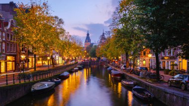 Altın sonbahar yaprakları, alacakaranlıkta sakin sulara yansıyan Amsterdam 'ın resim gibi kanallarını çevreleyen ağaçları süslüyor. Ağaçlardaki Noel ışıkları şehirde güzel bir gece yaşatıyor.