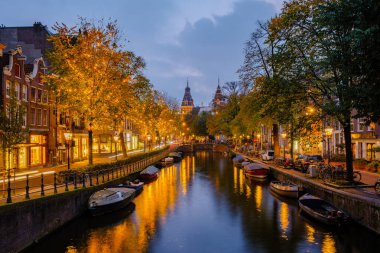 As twilight descends on Amsterdam, the charming canals reflect the golden hues of autumn trees. Shops glow warmly while boats float serenely, creating a magical atmosphere in this historic city. clipart