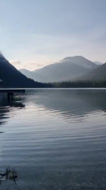 Durgun suların yükselen dağları yansıttığı gölün kenarında sabahın sessizliğini hissedin. Yumuşak bulutlar havada süzülüyor, Plansee Austria