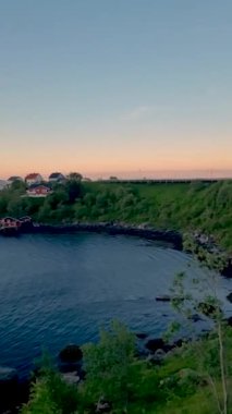 Güneş ufukta batarken, sakin sular alacakaranlıktaki ılık renkleri yansıtıyor. Koyun canlı manzarası arasında dinginliği davet ediyor. Rheine Lofoten Norveç