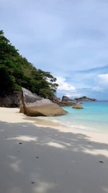 Similan Adası Tayland 'da rüzgarda hafifçe sallanan eşsiz kaya oluşumları, yumuşak beyaz kum ve canlı yeşil ağaçların bulunduğu sakin bir kumsalın güzelliğini hissedin.