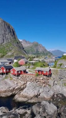 Geleneksel kırmızı kulübelerin dik dağlar ve sakin sulara karşı gururla durduğu Norveç Lofoten Hamnoy köyünün engebeli kıyı şeridini keşfedin.,