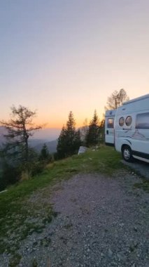 Güneşin batışı görkemli tepelerin ardında, rahat bir karavan yüksek ağaçların arasına kuruludur. Huzurlu manzara doğanın güzelliğini sergiliyor, Avusturya Alpleri 'ndeki büyük açık havada rahatlamaya ve maceraya davetiye çıkarıyor.