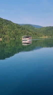 Canlı yeşilliklerle çevrili sakin, kristal berraklığında suların üzerinde süzülen bir tekne gibi huzurlu bir yolculuk yaşayın. Doğa, Gölün yumuşak dalgalarıyla uyumlu hale geldi: Plitvice Gölleri Hırvatistan