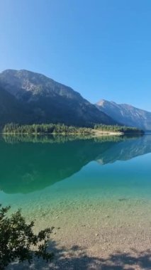 Turkuaz göl görkemli dağlarla çevrili. Sakin sular parlak gökyüzünü ve yemyeşil yeşilliği yansıtıyor. Huzurlu bir atmosfer yaratıyor. Rahatlamak için mükemmel. Plansee Avusturya